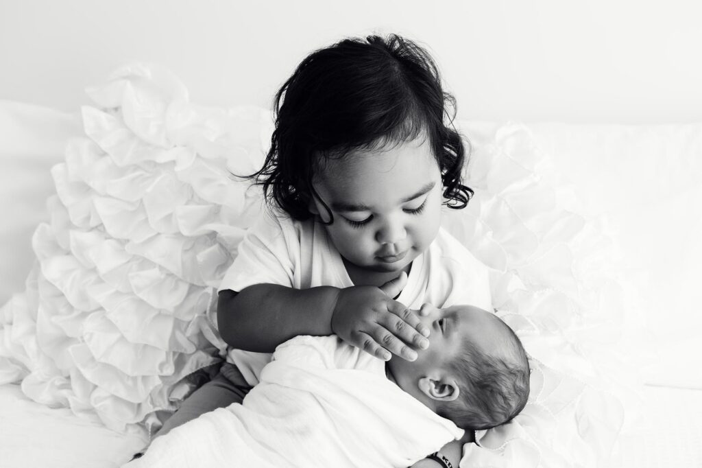 Black and white image of newborn being gently held by his big brother.