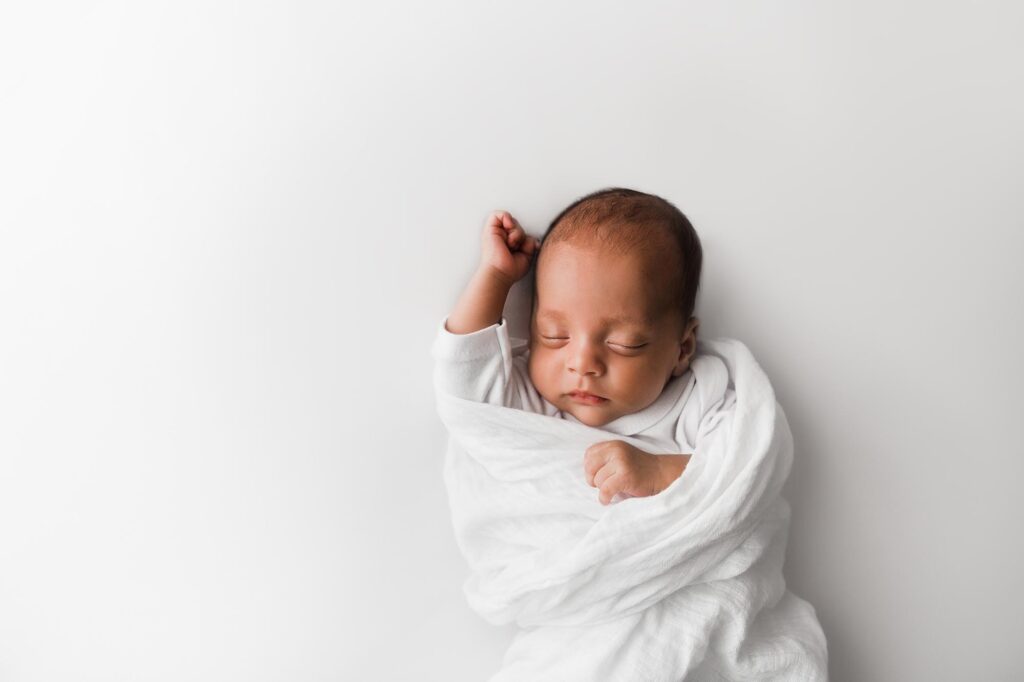 Newborn baby swaddles in white wrap.