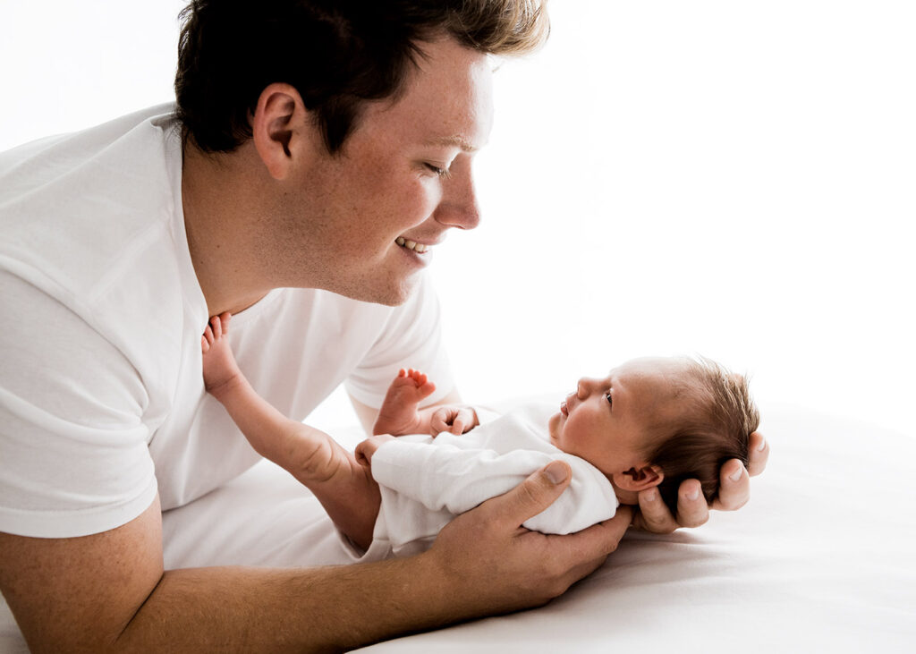 New dad looking into newborn babies eyes during photoshoot.