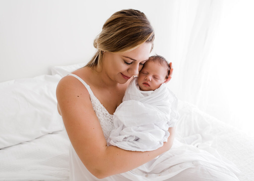 Mother holding newborn baby wrapped in a swaddle in her arms. 