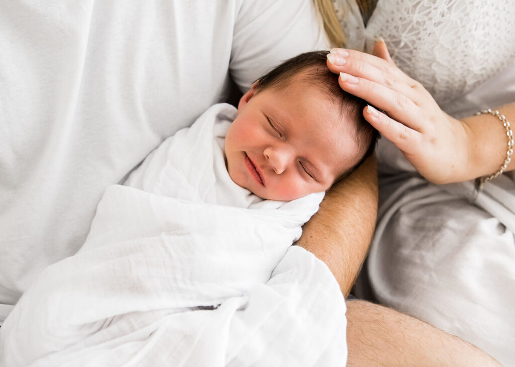 Close up of newborn babies face. The newborn has a slight smile on her face while mother is softly touching the babies head. 