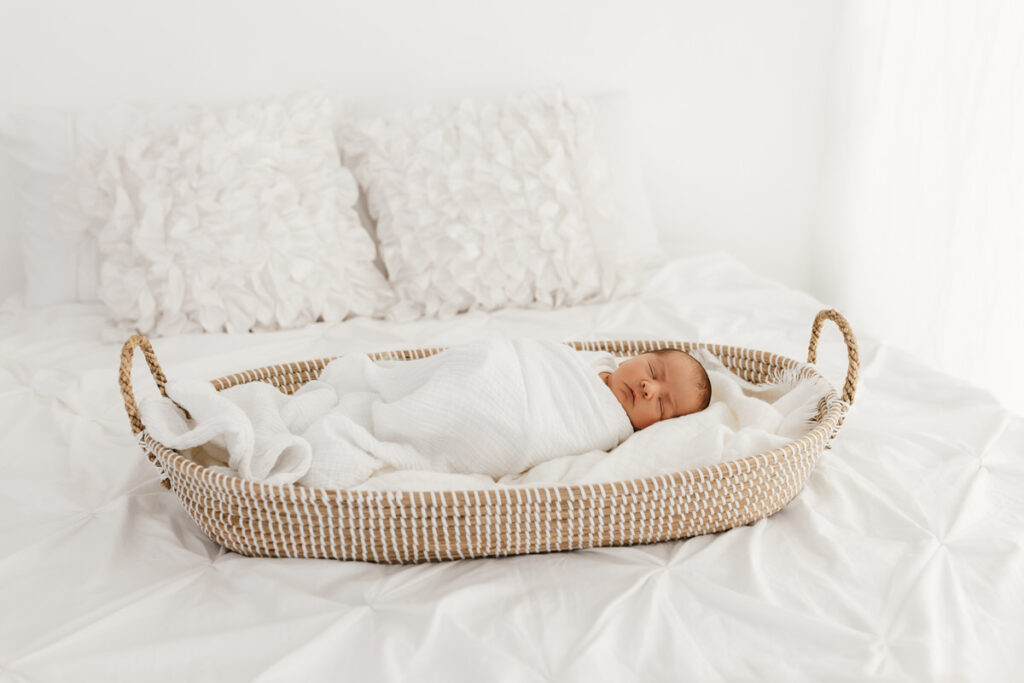 Newborn baby asleep laying in a woven Moses style basket.