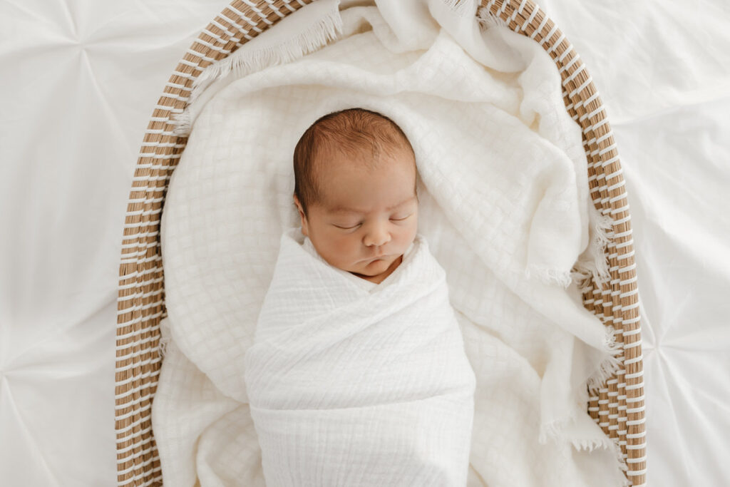 Newborn baby asleep laying in a woven moses style basket.