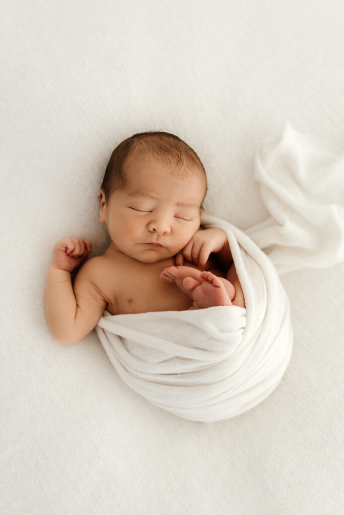 Newborn baby posed in white wrap during newborn photo shoot.