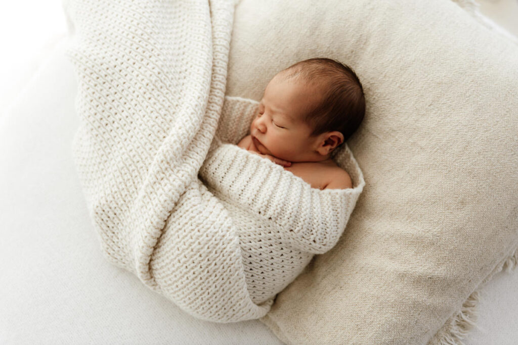 Newborn baby wrapped in a textured blanket laying on a pillow.