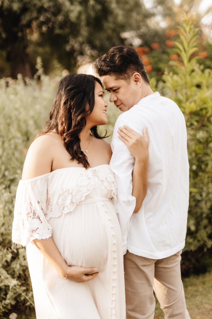 Couple expecting a baby posing in front of bushy shrubs during a maternity photo shoot at Umm Al Emarat Park in Abu Dhabi. 