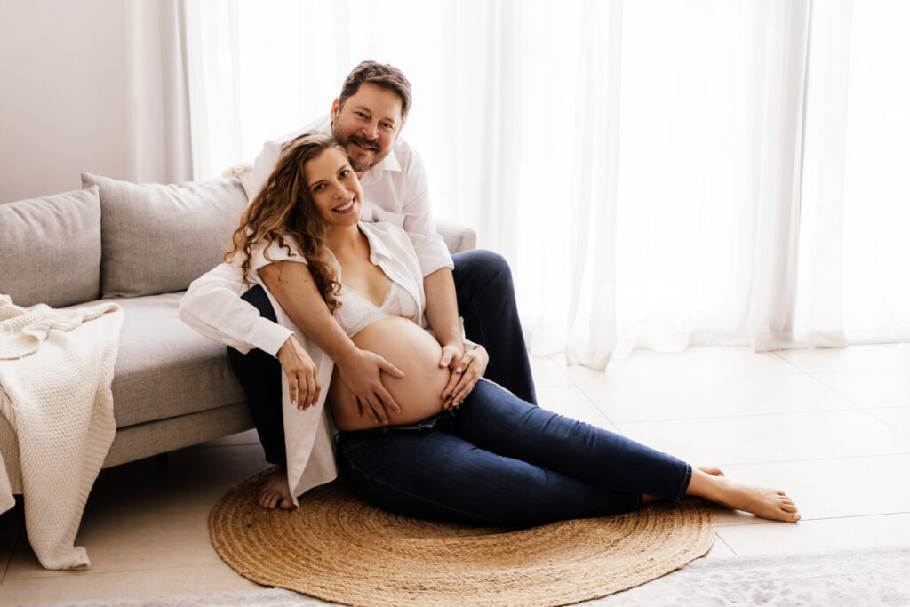 In the maternity photoshoot, the husband has his hands on his wife's baby bump, and they are both smiling in Abu Dhabi