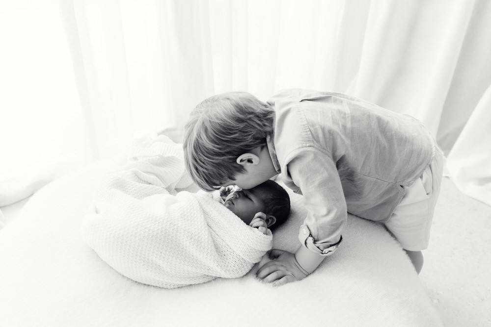 The older brother is lovingly kissing his little newborn baby in Abu Dhabi.